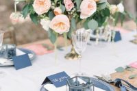 a stylish wedding tablescape with a blush wedding centerpiece, blue chargers and cards, pink menus and a neutral table runner