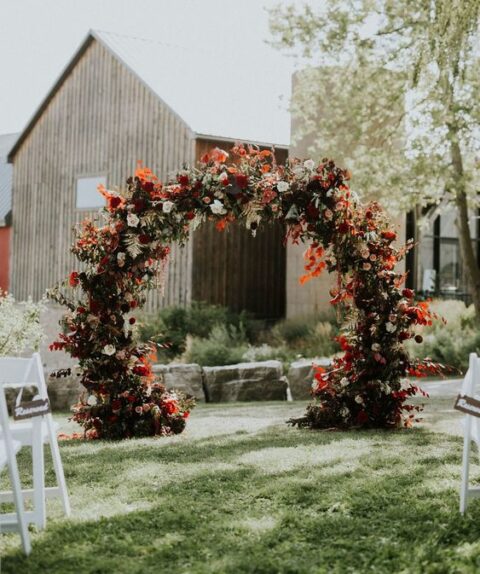 a super bold round fall wedding arch with bold blooms and white ones plus bold leaves and lots of foliage is a cool idea
