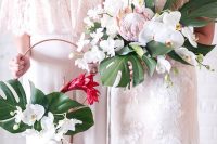 a tropical hoop wedding bouquet of white orchids, a red bloom and a couple of tropical leaves is a stylish and bold solution
