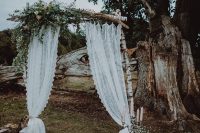 a very simple rustic fall wedding arch of branches, eucalyptus, baby’s breath and lace curtains plus candles around is amazing