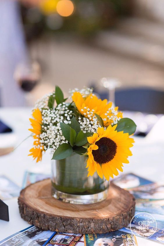 a wedding centerpiece of sunflowers, foliage and baby's breath in a glass is a simple and cool idea for a rustic wedding