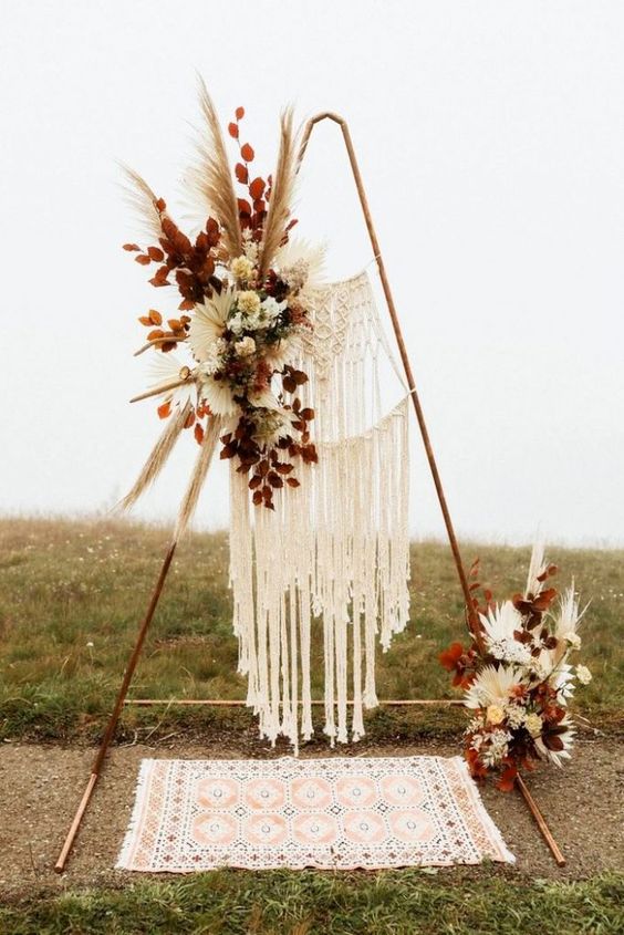 an amazing boho fall wedding arch with macrame, white and peachy blooms, dried leaves, pampas grass and dried fronds