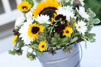 an amazing fall wedding centerpiece in a bucket,w ith sunflowers, white gerberas, greenery and some dark blooms