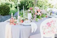 an elegant English garden wedding tablescape with a lilac tablecloth and neutral napkins, a chic peachy and pink rose centerpiece, tall candles and peaches on the table
