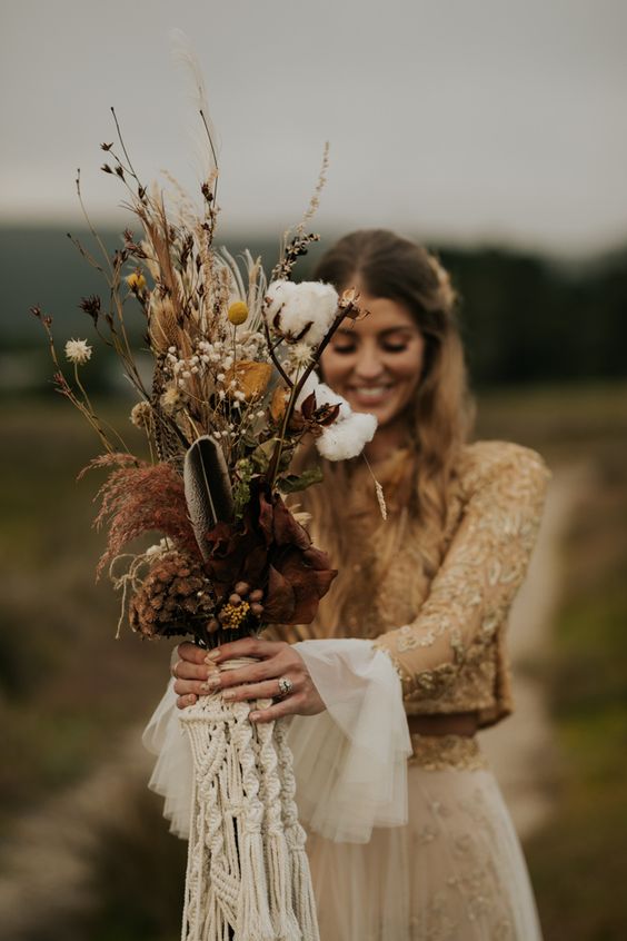 an organic boho fall wedding bouquet with cotton, billy balls, feathers, twigs and blooms plus a macrame wrap is a cool solution