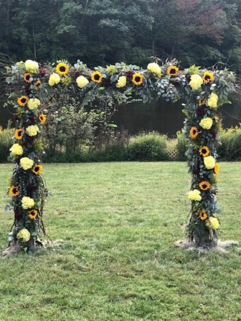 an outdoor wedding arch beautifully decorated with sunflowers, eucalyptus, hydrangea and roses is a pretty rustic wedding idea