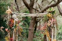 an unusual boho rustic wedding arch of branches, greenery, dried fall leaves, air plants, succulents is a very fresh and bold idea for the fall