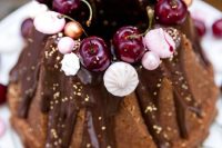 21 a chocolate bundt wedding cake with chocolate drip, gold leaf, fresh cherries, meringues and beads is a lovely and glam idea