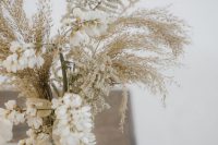 a beautiful and ethereal wedding centerpiece of a vintage vase, some white blooms, lunaria and dried grasses is a lovely idea