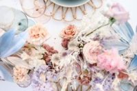 a beautiful iridescent wedding table setting with wooden placemats, bold dried blooms and leaves, pastel plates and pink cutlery is chic