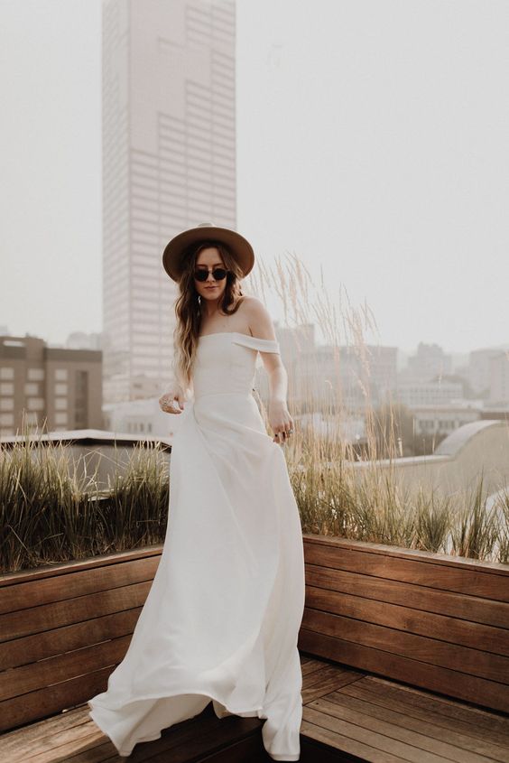 a beautiful modern plain off the shoulder wedding dress paired with a neutral hat and sunglasses is amazing