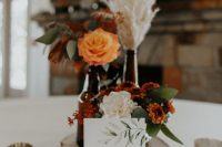 a boho fall wedding centerpiece of a wood slice, neutral and bold blooms, pampas grass, greenery and candles around is amazing for the fall