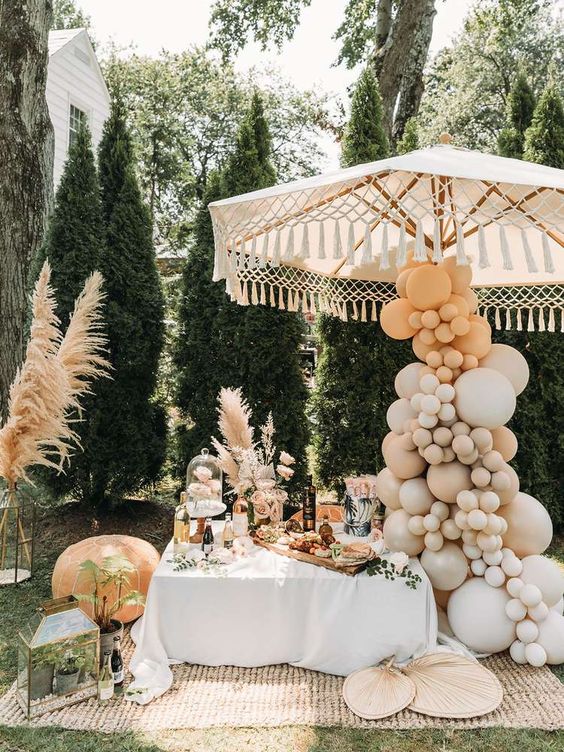a boho wedding food station styled with pampas grass, with neutral balloons covering an umbrella, with candle lanterns and fans is cool