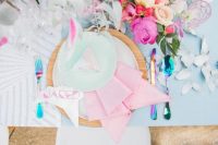 a bold iridescent wedding place setting with a plywood charger, a pink napkin and a mint plate, a blue tablecloth, bold blooms and iridescent cutlery