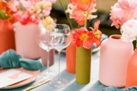 a bright bridal shower table setting with muted color vases, pink and red blooms, a blue tablecloth and napkins, pink plates is a chic idea