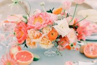 a bright bridal shower tablescape with a blue tablecloth, pink napkins, orange and pink blooms, citrus and floral cakes is a lovely idea