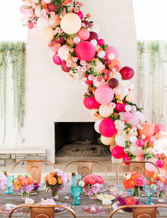 a bright bridal shower tablescape with bold blooms, glasses, napkins and a fantastic balloon garland with bold blooms and greenery is amazing