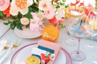 a bright bridal shower tablescape with pink plates and napkins, with pink, red and peachy blooms plus greenery, gold edge glasses