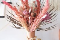 a bright dried flower and grass wedding centerpiece of a terracotta vase, bright fronds, leaves and grasses and plus some flowers