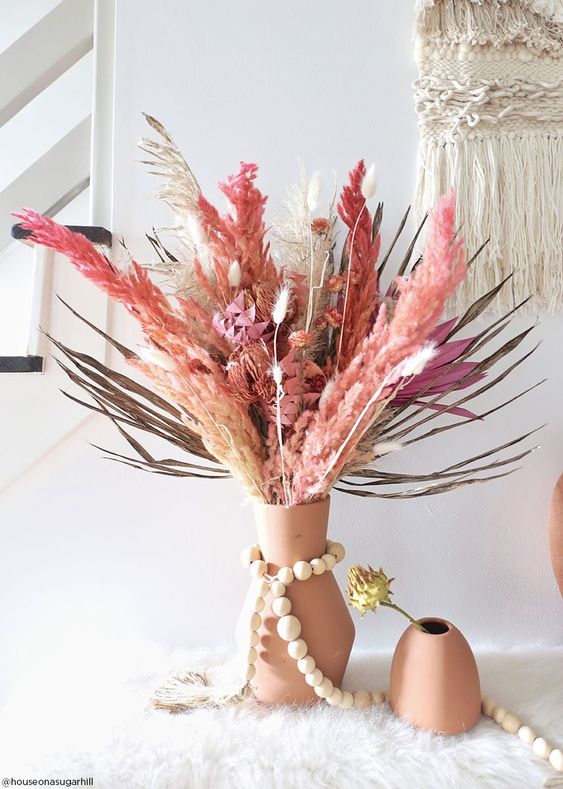 a bright dried flower and grass wedding centerpiece of a terracotta vase, bright fronds, leaves and grasses and plus some flowers