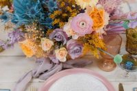 a bright wedding tablescape with an iridescent wedding floral arrangement, a pink charger, gold cutlery and colored glasses for an iridescent wedding