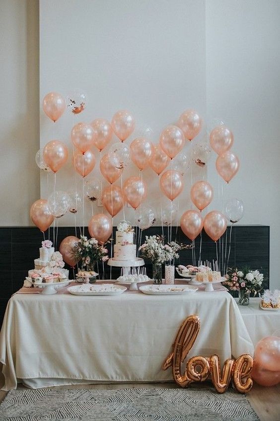 a chic and cool wedding dessert table with peachy and clear balloons, with pink and white florals and gold letter balloons is all cool