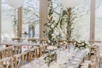 a chic farmhouse-inspired wedding reception with trestle tables and wooden chairs, burlap runners, pastel and neutral blooms and white balloons over the table