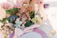 a chic iridescent wedding tablescape with a purple charger, blush, blue and lilac blooms, a clear and purple glass