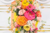 a colorful bridal shower tablescape with an orange table runner, a colorful floral centerpiece, pink napkins and colored glasses is cool