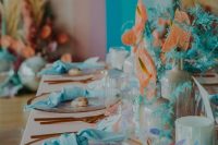 a colorful iridescent wedding tablescape with turquoise napkins, coral and turquoise blooms, blue and blush touches
