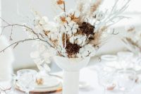 a cozy tall wedding centerpiece of cotton, twigs, branches and dried blooms is a beautiful idea for a modern wedding