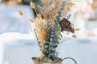 a creative wedding centerpiece of a metal jug, bunny tails, eucalyptus and lotus is a very non-traditional arrangement to rock in the fall