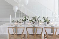 a delicate and minimalist wedding tablescape with white blooms and greenery, candles, grey porcelain and white balloons is wow