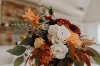 a fall boho wedding centerpiece of a wood slice, a jar with white, rust and burgundy blooms, greenery and fall leaves is amazing