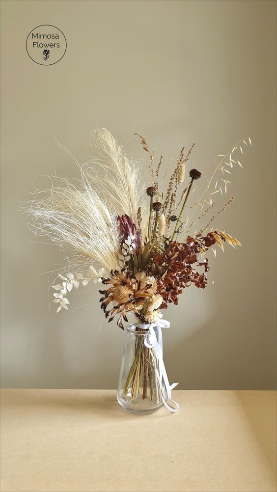 a fall boho wedding centerpiece of grasses, dried blooms and dried leaves and foliage is a pretty and bold decor idea