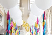 a fun and colorful wedding ceremony space with white balloons and colorful tassels, with gold balloon letters and sheer chairs