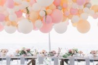a fun wedding reception space with a colorful balloon garland over the table with bold blooms, greenery and pastel florals is amazing