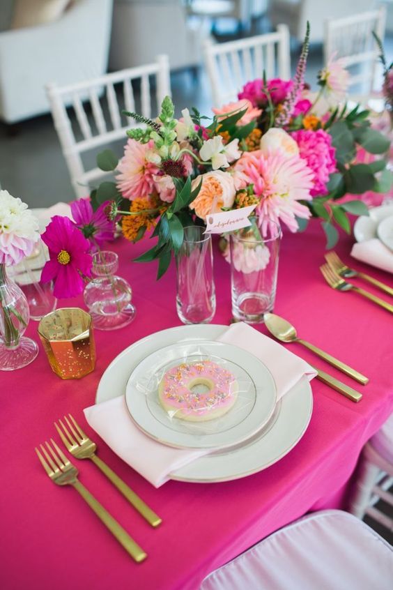 a hot pink bridal shower tablescape with a hot pink tablecloth and blooms, with greenery, gold touches and white porcelain is amazing