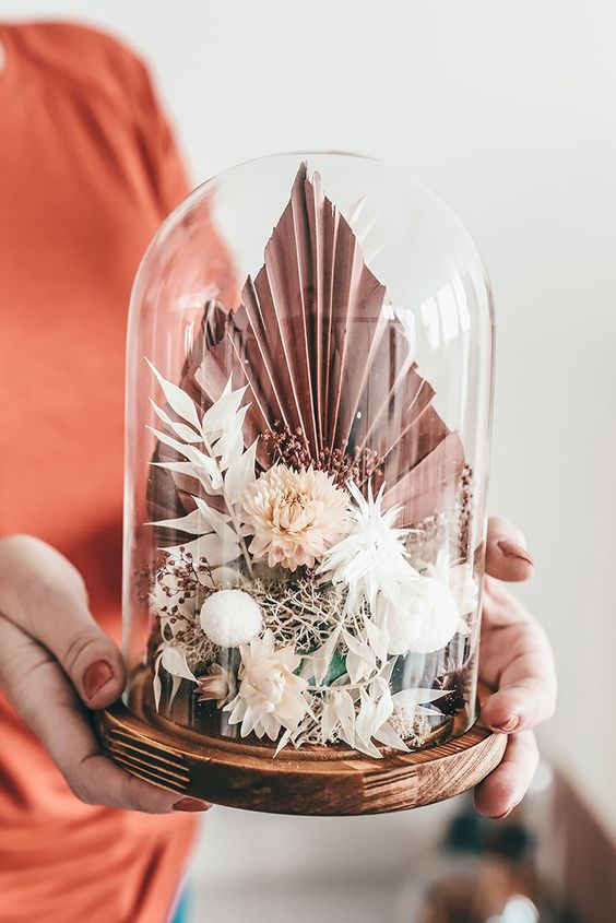 a lovely cloche wedding centerpiece of dried pink and white blooms, pink fronds and some grasses is a gorgeous idea