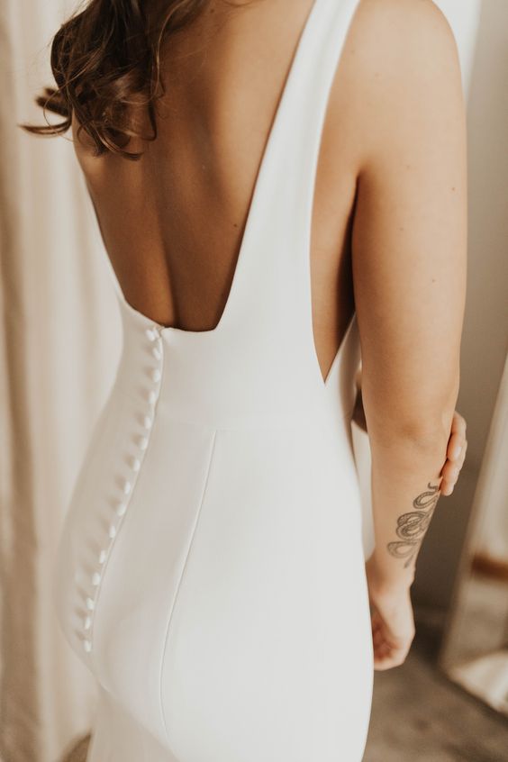 a minimalist plain sheath wedding dress with a cutout back on buttons and depe cut sides looks incredibly sexy and bold