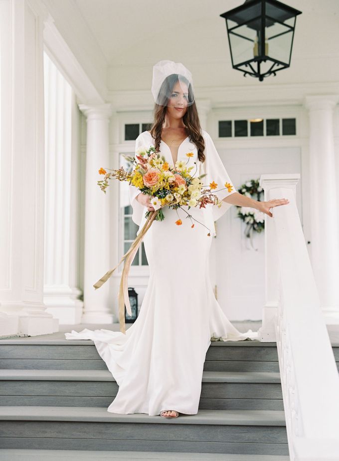 a plain white wedding dress with a covered plunging neckline, wide bell sleeves and a train plus a retro veil for a frehs look
