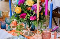 a super bright bridal shower tablescape with a peachy runner, colorful candles, pink napkins and super bright glasses plus bold and colorful blooms and greenery