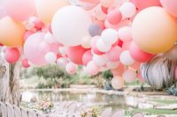 a vintage and refined wedding tablescape with a whitewashed table and chairs, pink blooms, a bright oversized balloon garland over it for a playful touch