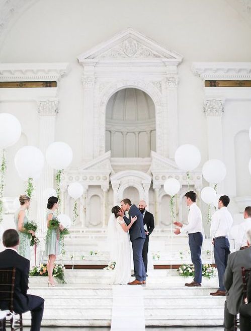 a wedding ceremony space with white balloons with greenery, white and pastel blooms is a very chic and cool and fresh idea