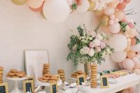 a wedding sweets table with white and pastel blooms plus greenery, pink, white, coral and gold balloons and blooms over it is amazing