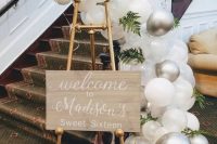 a welcome sign on gold legs, with clear, white and silver balloons and greenery is a very pretty and chic idea to rock