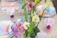 an iridescent wedding tablescape with a white sequin tablecloth, pink, lilac and white blooms, disco balls, iridescent plates and sugar crystal candies