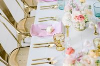 an iridescent wedding tablescape with pink and lilac napkins, pink, blush, lilac and peachy blooms, gold glasses and cutlery