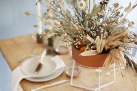 an organic wedding centerpiece of a terracotta vase, with dried blooms, berries, grasses and whitewashed leaves is a chic idea