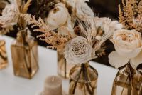cool boho fall wedding centerpiece of dried blooms, branches, leaves, grasses and peachy and light pink blooms, with colored vases and a neutral candle